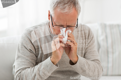 Image of sick senior man with paper wipe blowing his nose