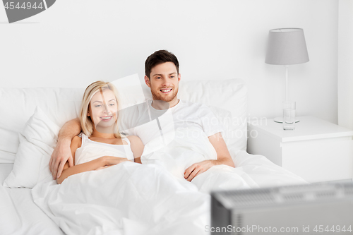 Image of happy couple lying in bed at home and watching tv