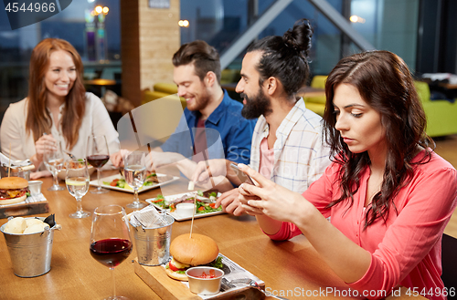 Image of bored woman messaging on smartphone at restaurant