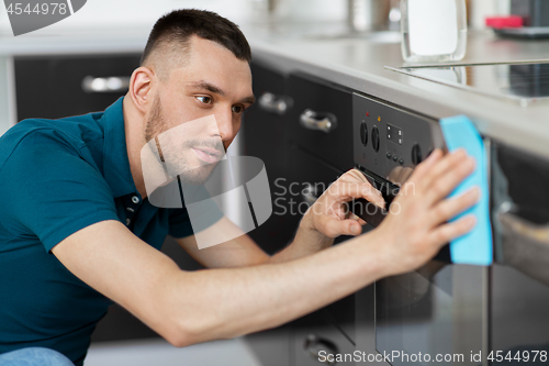 Image of man with rag cleaning oven door at home kitchen