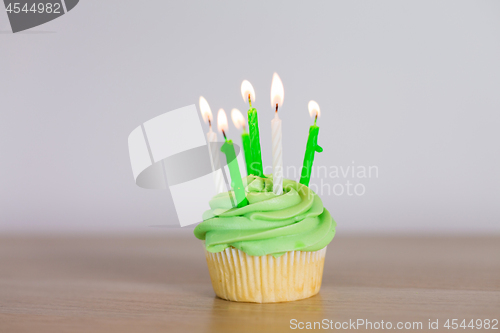 Image of green cupcake with six burning candles on table