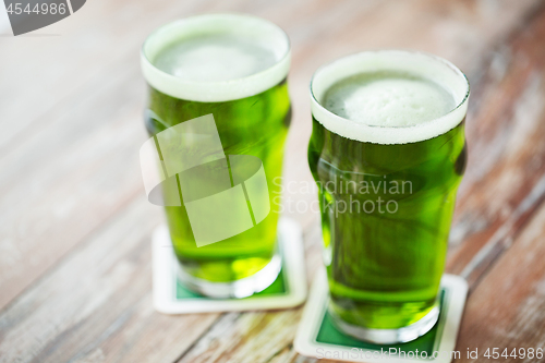 Image of two glasses of green beer on wooden table