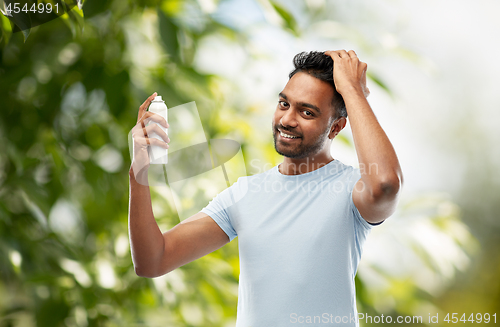 Image of smiling indian man applying hair spray over gray