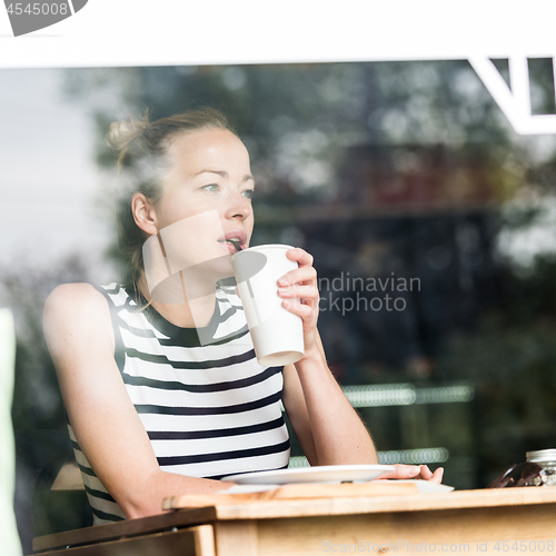 Image of Young caucasian woman sitting alone in coffee shop thoughtfully leaning on her hand, looking trough the window