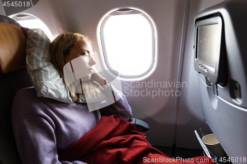 Image of Tired blonde casual caucasian lady sleepin on seat while traveling by airplane. Commercial transportation by planes.