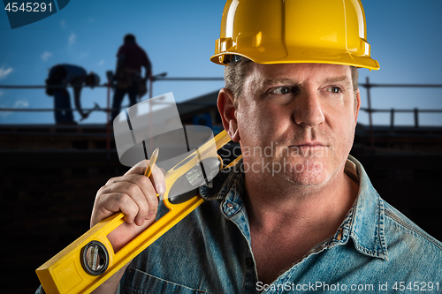 Image of Serious Contractor in Hard Hat Holding Level and Pencil At Const