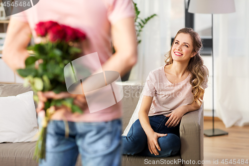 Image of woman looking at man with bunch of flowers at home