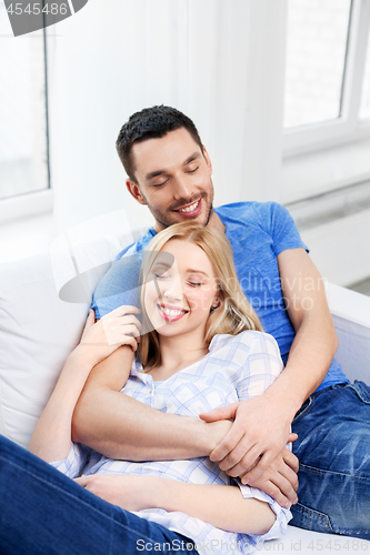 Image of happy couple sitting on sofa and hugging at home