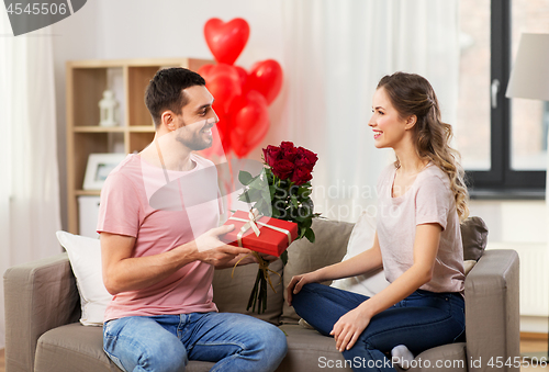 Image of happy man giving woman flowers and present at home