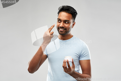 Image of happy indian man applying cream to face