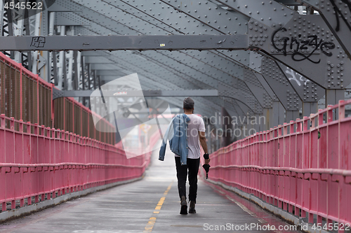 Image of Rear view of unrecognizable stylish young man carrying jeans jacket over his shoulder walking on Williamsburg Bridge, Brooklyn, New York City.