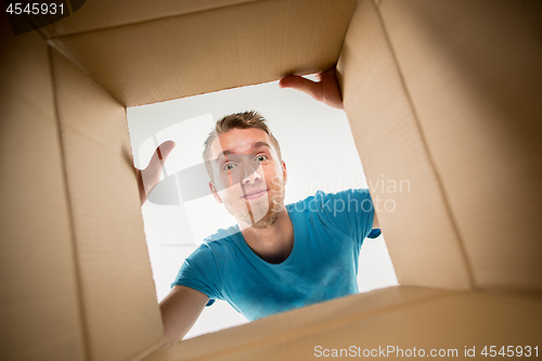 Image of Man smiling, unpacking and opening carton box and looking inside