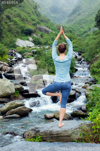 Image of Woman in yoga asana Vrikshasana tree pose at waterfall outdoors