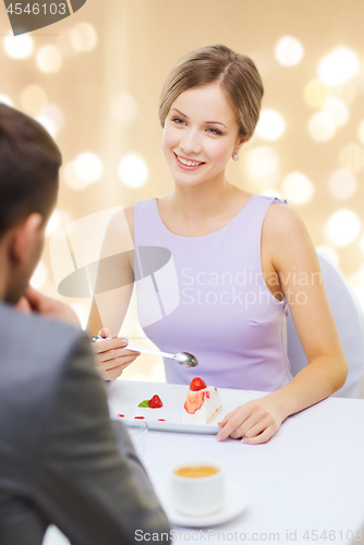 Image of woman looking at man and eating cake at restaurant