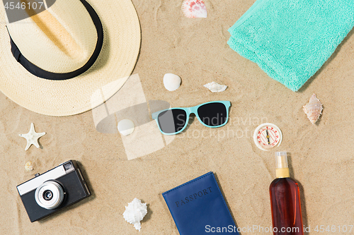 Image of camera, passport, sunglasses and hat on beach sand