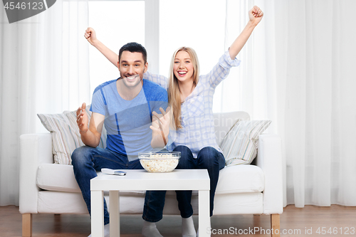 Image of happy couple with popcorn watching tv at home