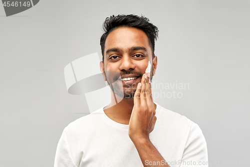 Image of happy indian man applying cream to face