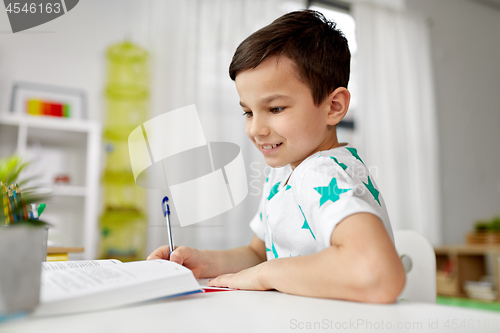 Image of student boy with book writing to notebook at home