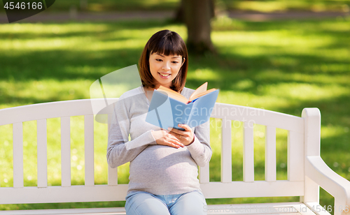 Image of happy pregnant asian woman reading book at park