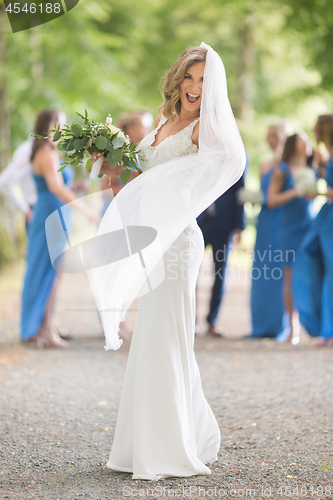 Image of Full length portrait of beautiful sensual young blond bride in long white wedding dress and veil, holding bouquet outdoors in natural background