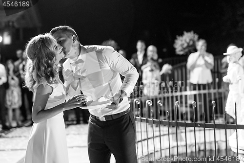 Image of Happy bride and groom getting messy eating piece of wedding cake by their hands after cutting it.