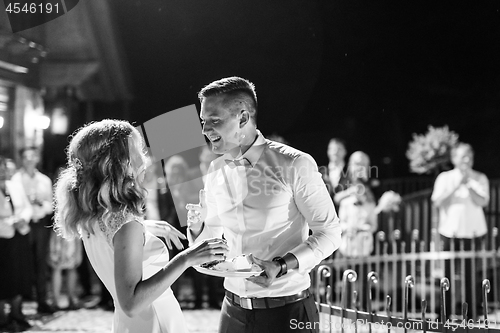 Image of Happy bride and groom getting messy eating piece of wedding cake by their hands after cutting it.