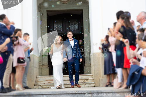 Image of Newlyweds exiting the church after the wedding ceremony, family and friends celebrating their love with the shower of soap bubbles, custom undermining traditional rice bath