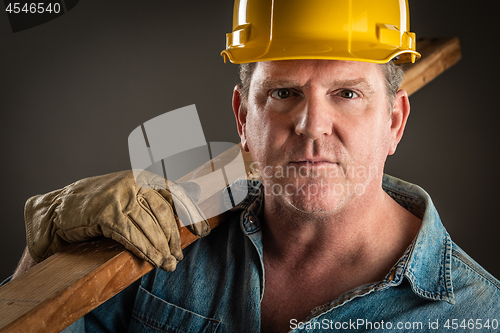 Image of Serious Contractor in Hard Hat Holding Plank of Wood With Dramat