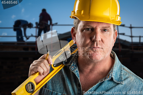 Image of Serious Contractor in Hard Hat Holding Level and Pencil At Const