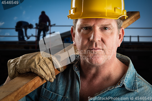 Image of Serious Contractor in Hard Hat Carrying Wood Plank At Constructi