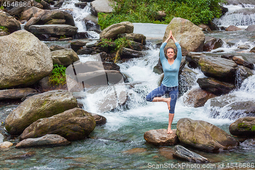 Image of Woman in yoga asana Vrikshasana tree pose at waterfall outdoors