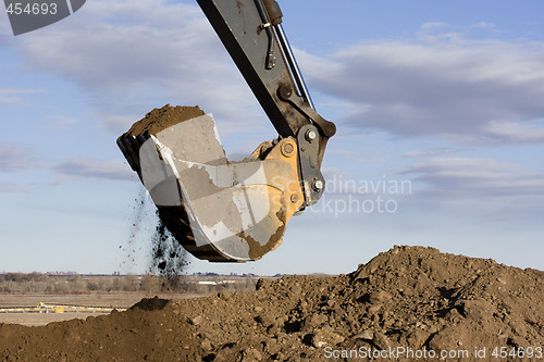 Image of Excavator arm and scoop digging dirt at construction site