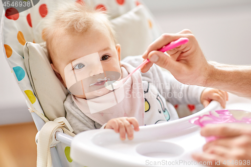 Image of father feeding baby sitting in highchair at home