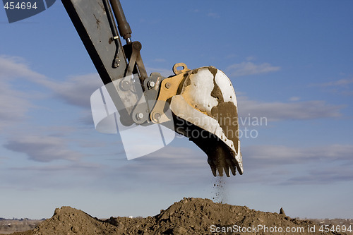 Image of Excavator arm and scoop digging dirt at construction site
