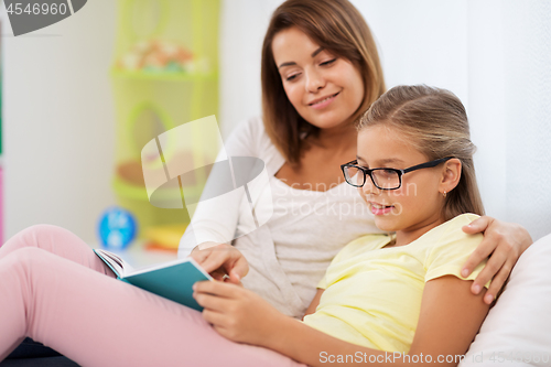 Image of happy girl with mother reading book at home