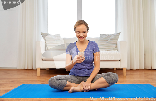 Image of woman with smartphone doing yoga at home