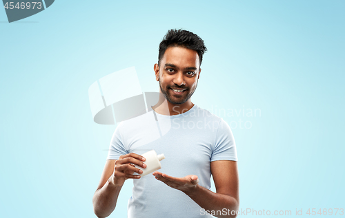 Image of happy indian man applying lotion to his hand