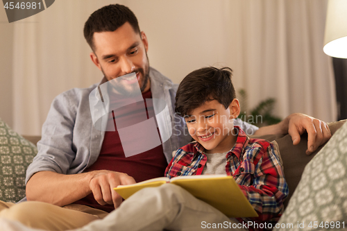 Image of happy father and son reading book sofa at home