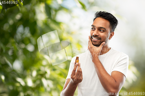 Image of smiling indian man applying grooming oil to beard