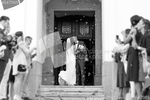 Image of Newlyweds kissing while exiting the church after wedding ceremony, family and friends celebrating their love with the shower of soap bubbles, custom undermining traditional rice bath