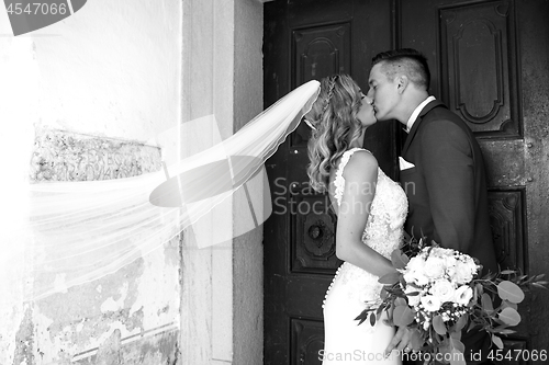 Image of The Kiss. Bride and groom kisses tenderly in front of church portal.