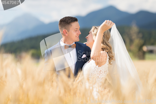 Image of Groom hugs bride tenderly while wind blows her veil in wheat field somewhere in Slovenian countryside.