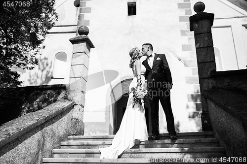 Image of The Kiss. Bride and groom kisses tenderly on a staircase in front of a small local church.