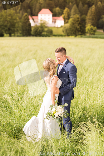 Image of Newlyweds hugging tenderly in meadow in front of Strmol castle in Slovenian countryside.