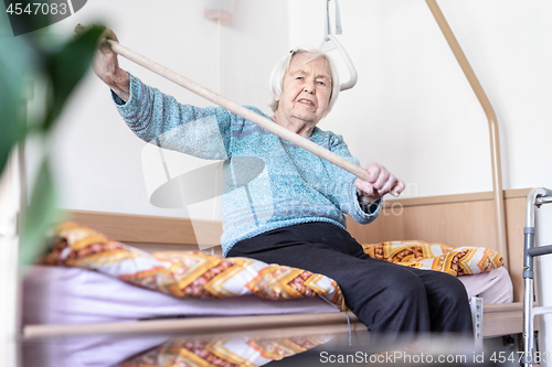 Image of Elderly 96 years old woman exercising with a stick sitting on her bad.