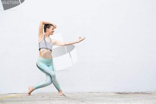 Image of Fit sporty active girl in fashion sportswear doing yoga fitness exercise in front of gray wall, outdoor sports, urban style