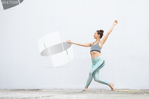 Image of Fit sporty active girl in fashion sportswear doing yoga fitness exercise in front of gray wall, outdoor sports, urban style