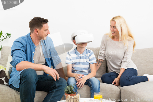 Image of Happy family at home on living room sofa having fun playing games using virtual reality headset