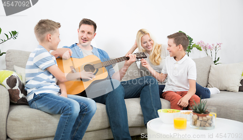 Image of Happy caucasian family smiling, playing guitar and singing songs together at cosy modern home
