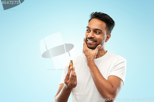 Image of smiling indian man applying grooming oil to beard